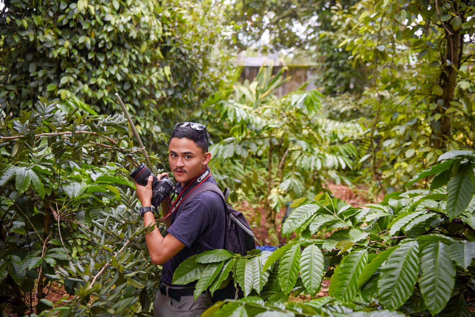 Anton Delgado Anton Delgado stands in a forest holding a camera.