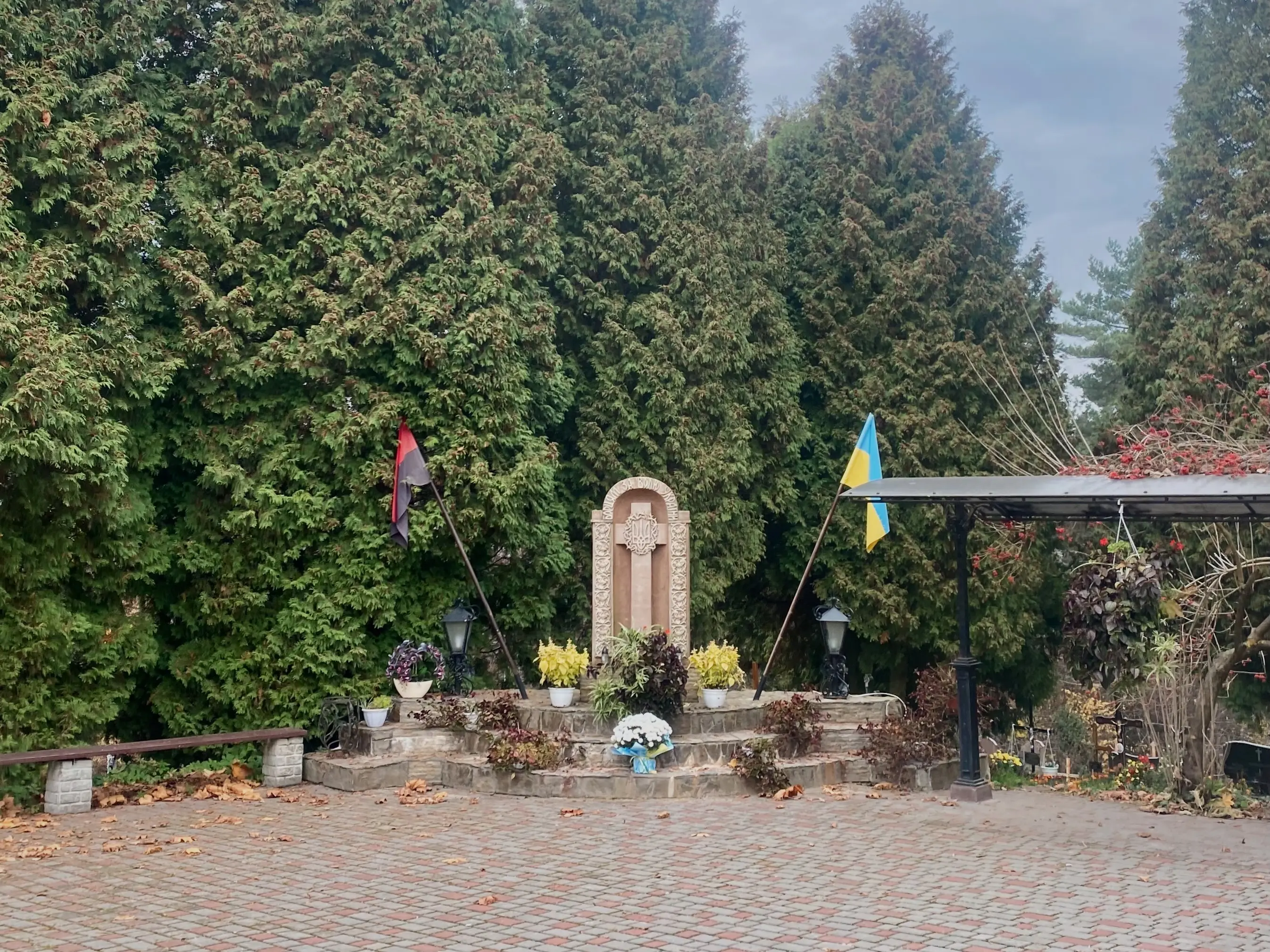 Photo 3.jpg n Stradch, Ukraine, a cross is flanked by the national flag of Ukraine, right, and the flag of the Ukrainian Insurgent Army, left. The latter’s colors represent those of the first as if covered in blood. Image by Madeleine Long. Ukraine, 2022.
