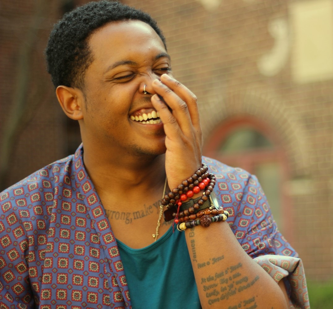 Photo of Danez Smith, partially covering their face while laughing.