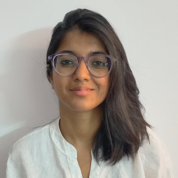 A woman with medium length hair and brown skin wearing a white shirt stands with a white background