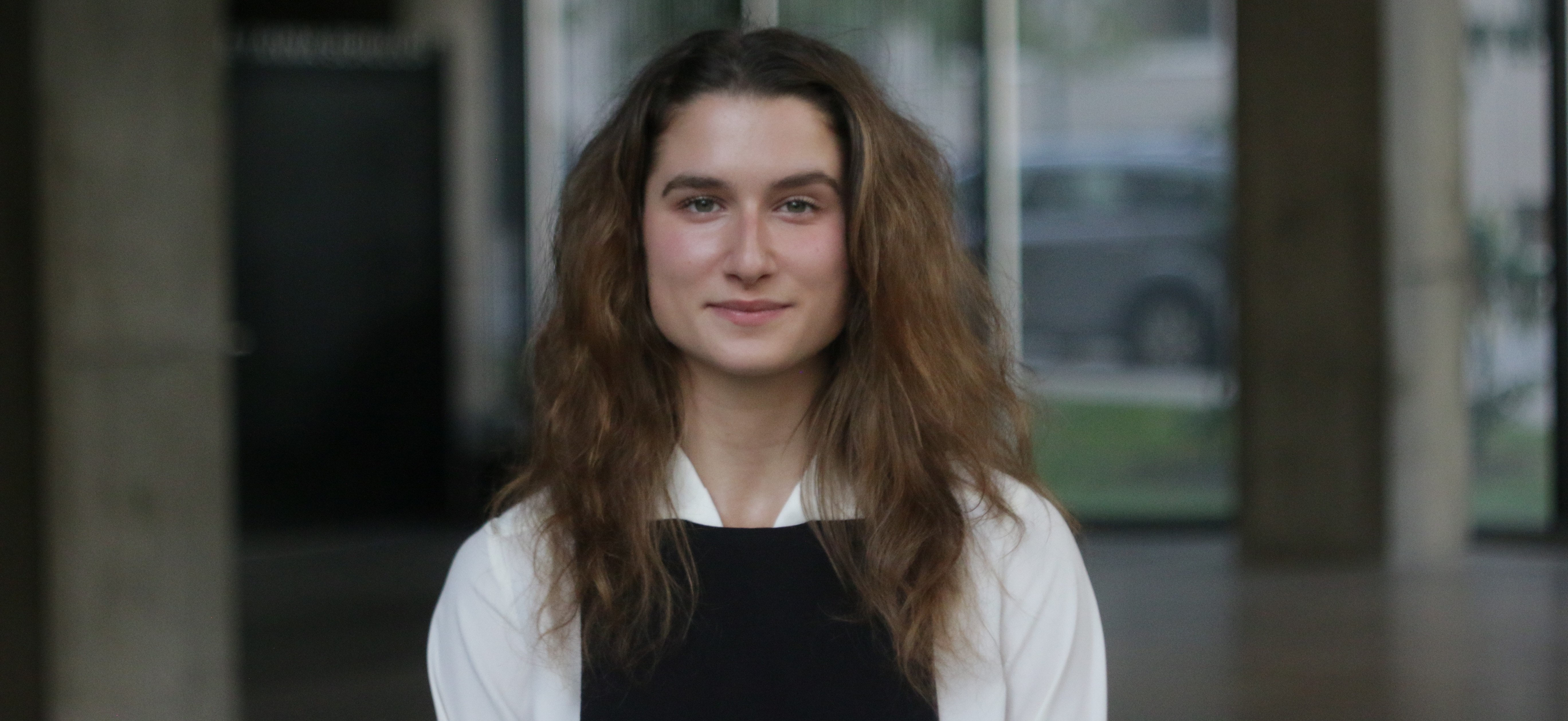 A woman with long light hair wears a white shirt with black overalls