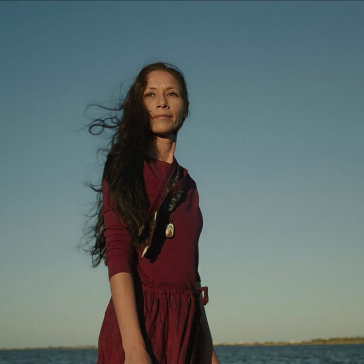 Woman in burgundy dress stands in front of setting sun