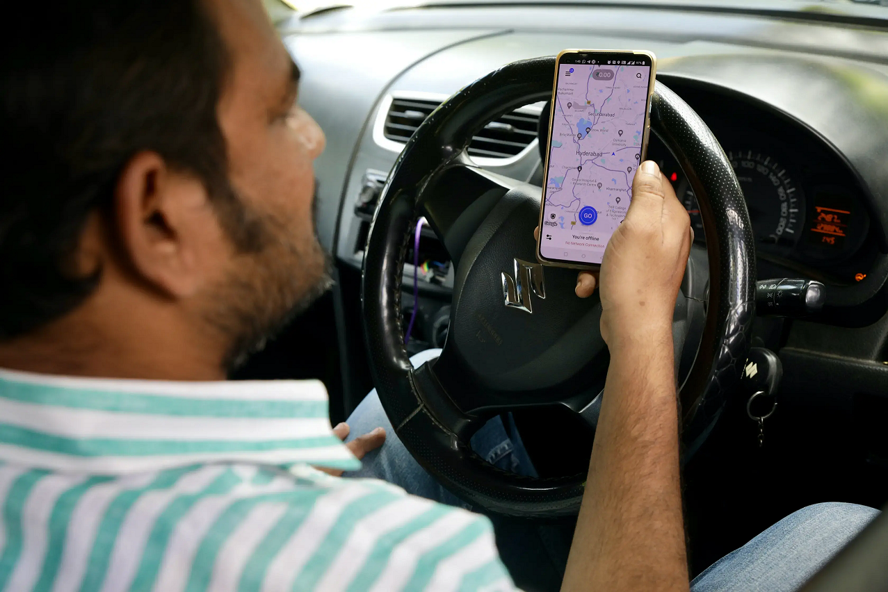 An uber driver checks the map on his phone while sitting at the wheel.