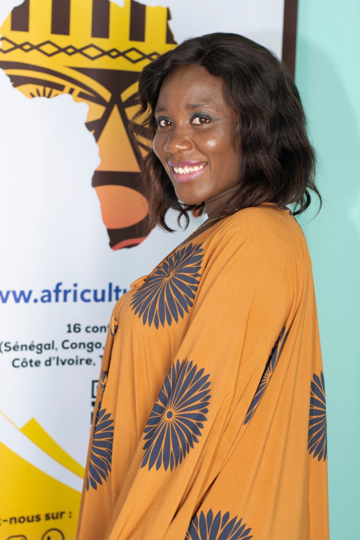 A woman smiles clad in a mustard dress against a flex standee with a map of Africa on it.