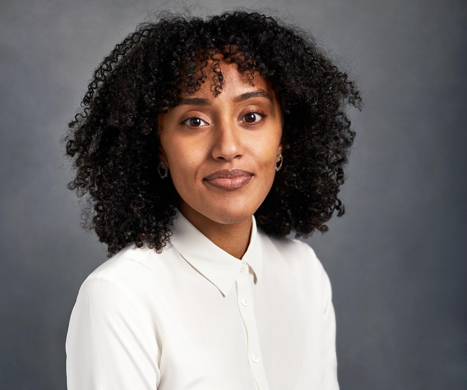 A woman with dark curly hair wearing a white button down shirt