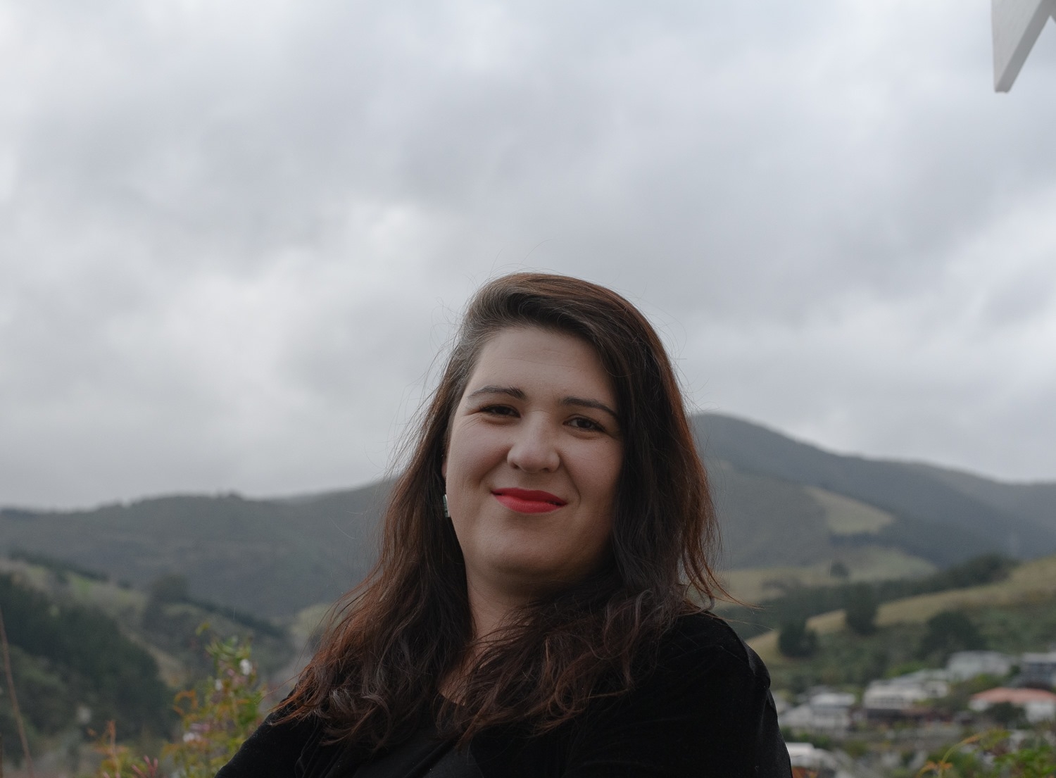 A woman with long dark hair smiles against a mountainous background
