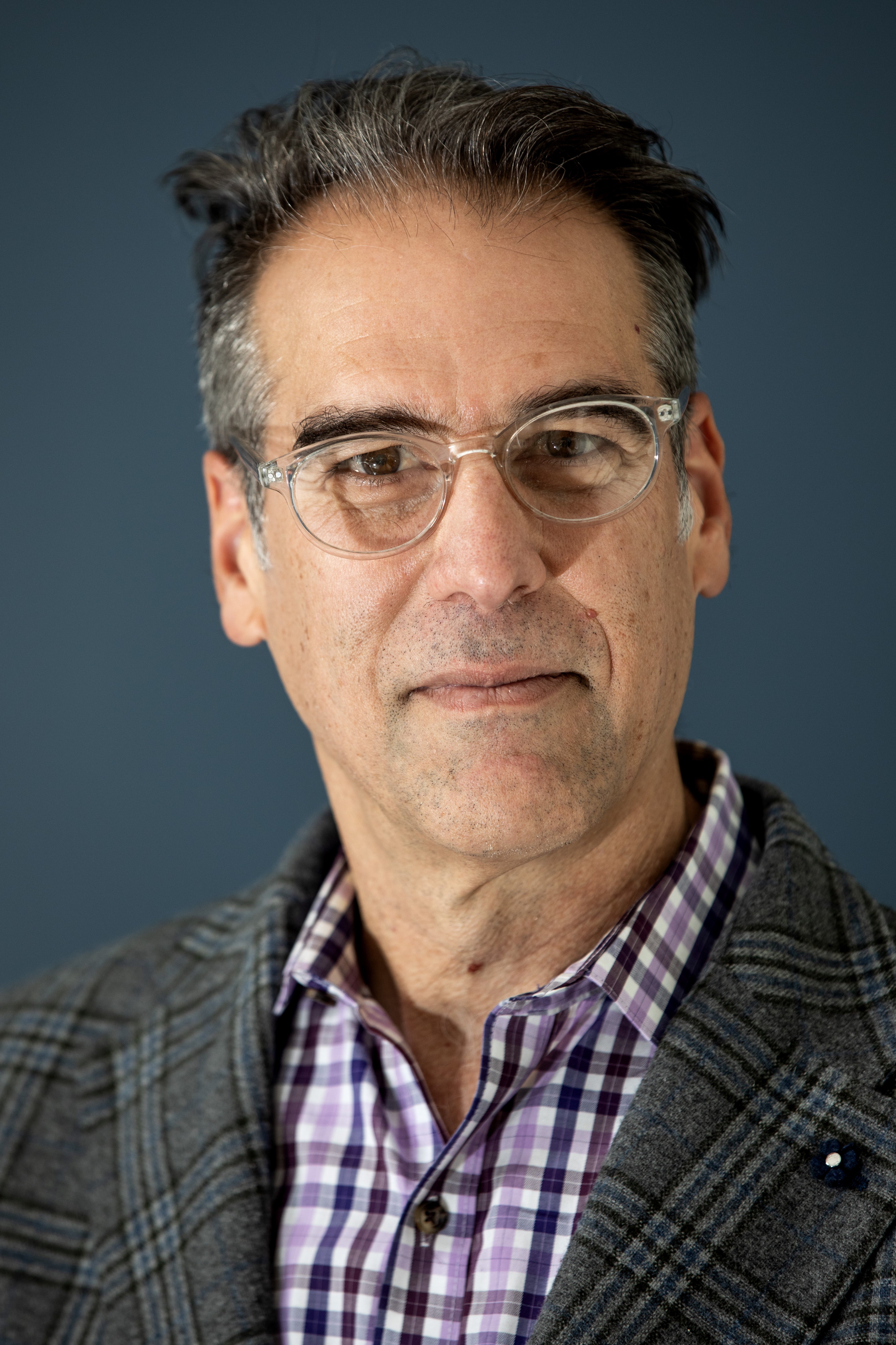 A man with short hair, glasses, wearing a plaid button down under a blazer