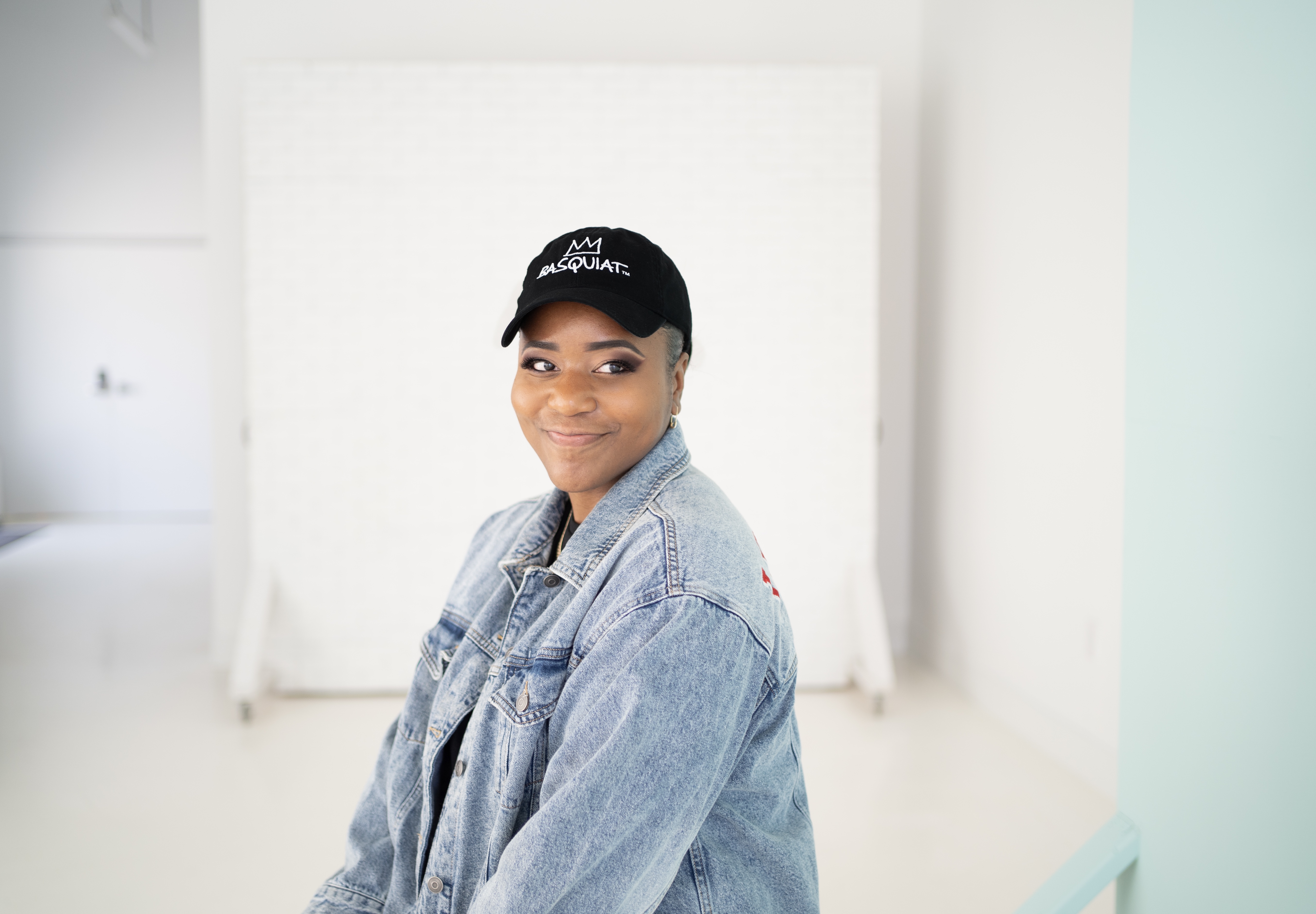 A woman wearing a black "Basquiat" baseball cap and a jean jacket