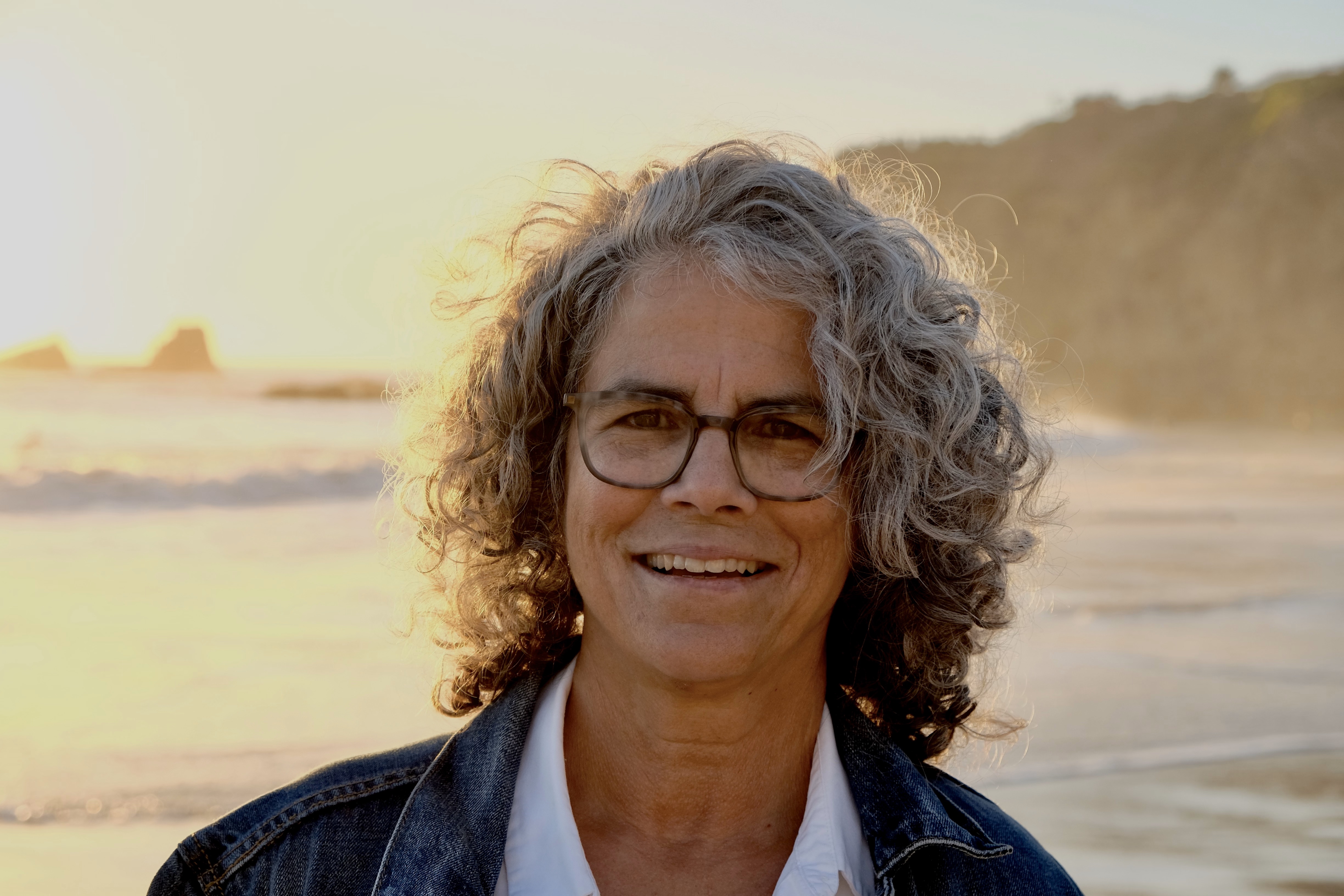 A woman with curly grey hair and glasses on a beach