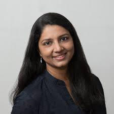 A woman with long dark hair smiles against a neutral background