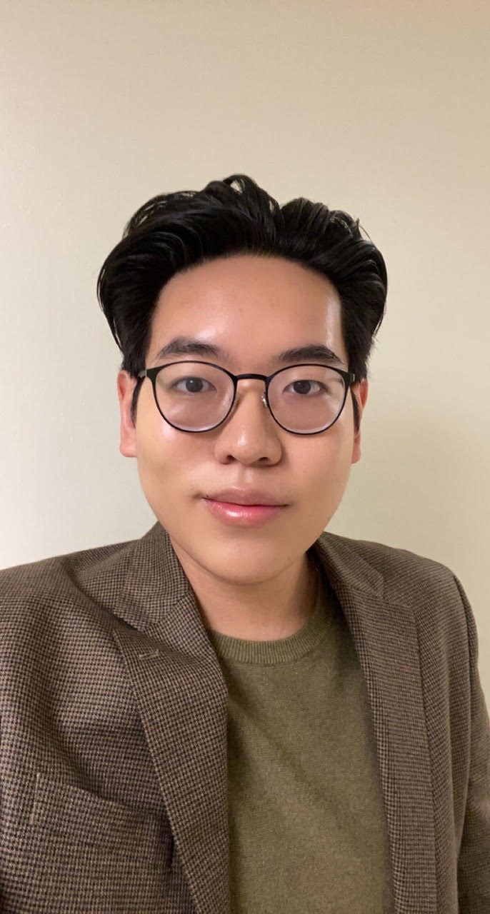 A man with short black hair wearing a green blazer and glasses