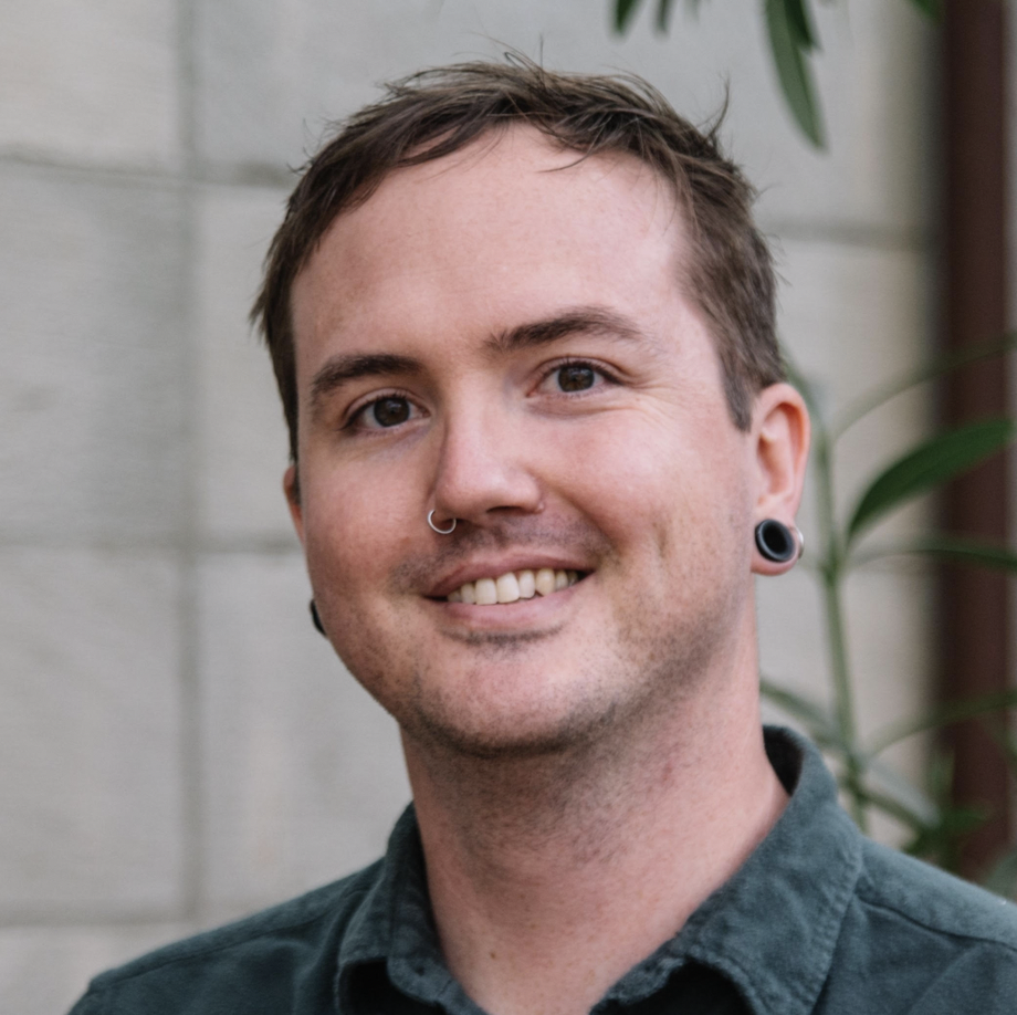 A smiling man with short dark hair wearing a green collared shirt