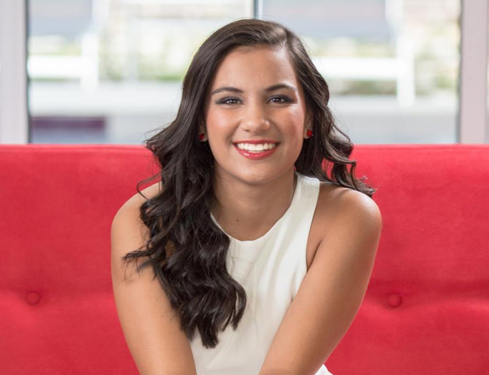 A woman with long dark hair wearing a white top sitting on a red couch