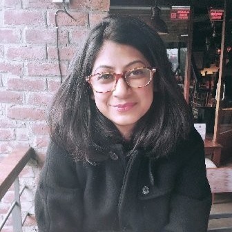 A woman with glasses and long dark hair wearing a black coat