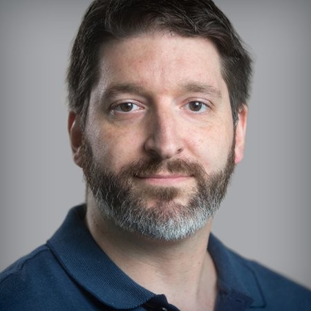 Headshot of a man with short dark hair wearing a navy button-down