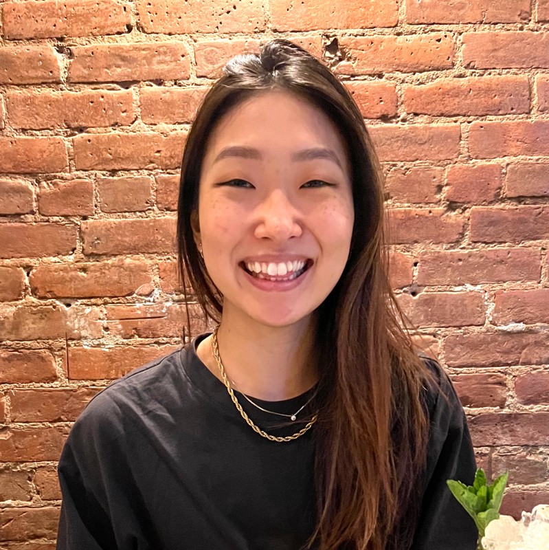 A woman with long straight hair wearing black against a brick background