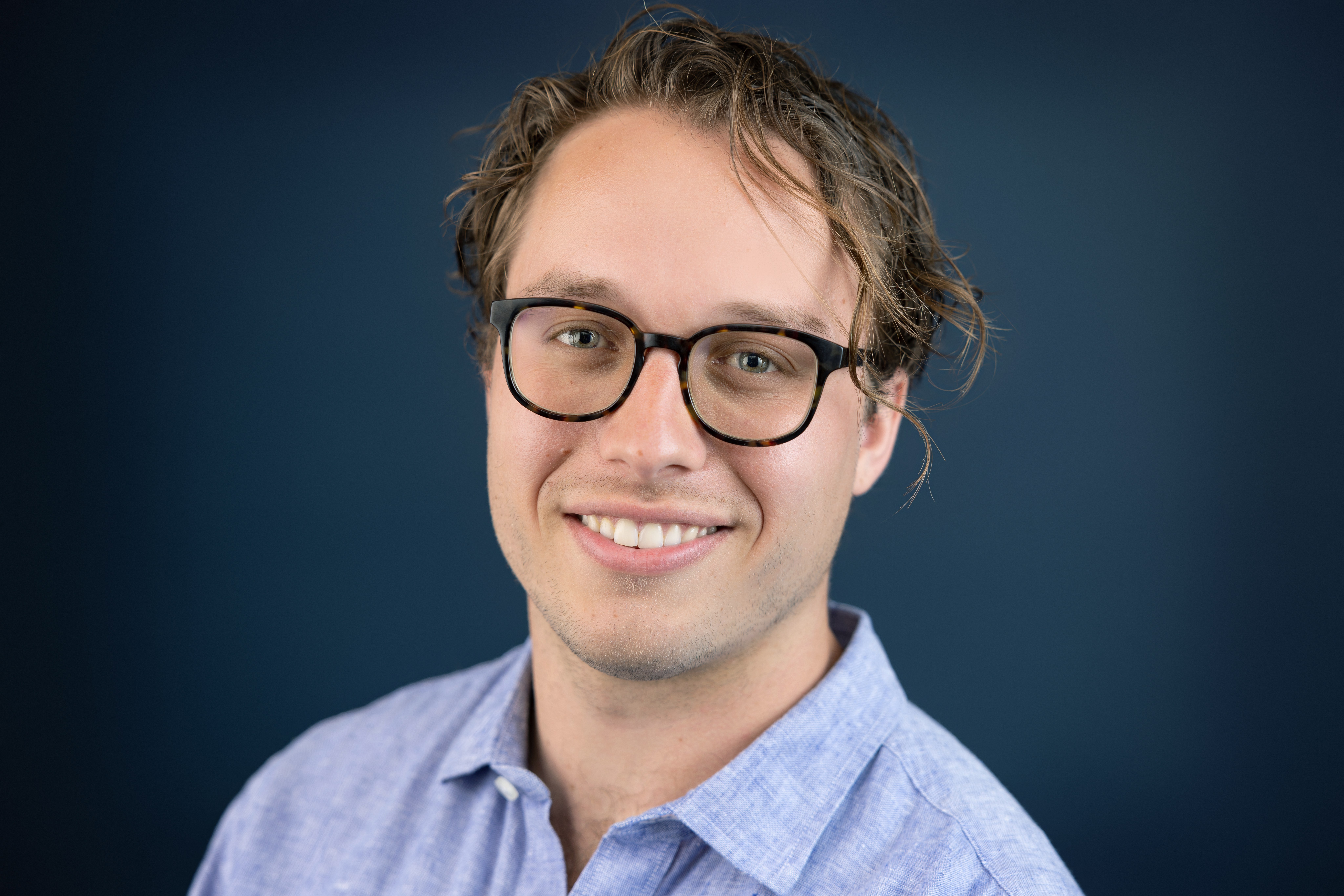 Headshot of James wearing glasses and a light blue collared shirt