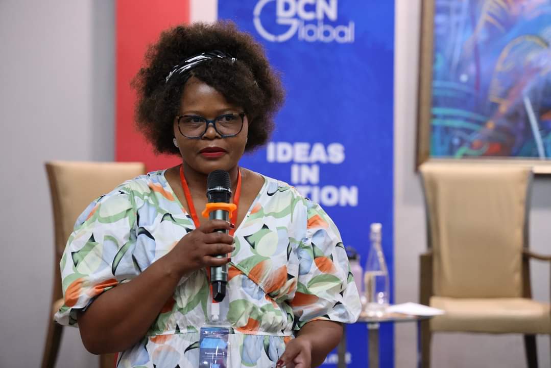 Pascalinah speaks at a conference wearing a patterned dress and glasses