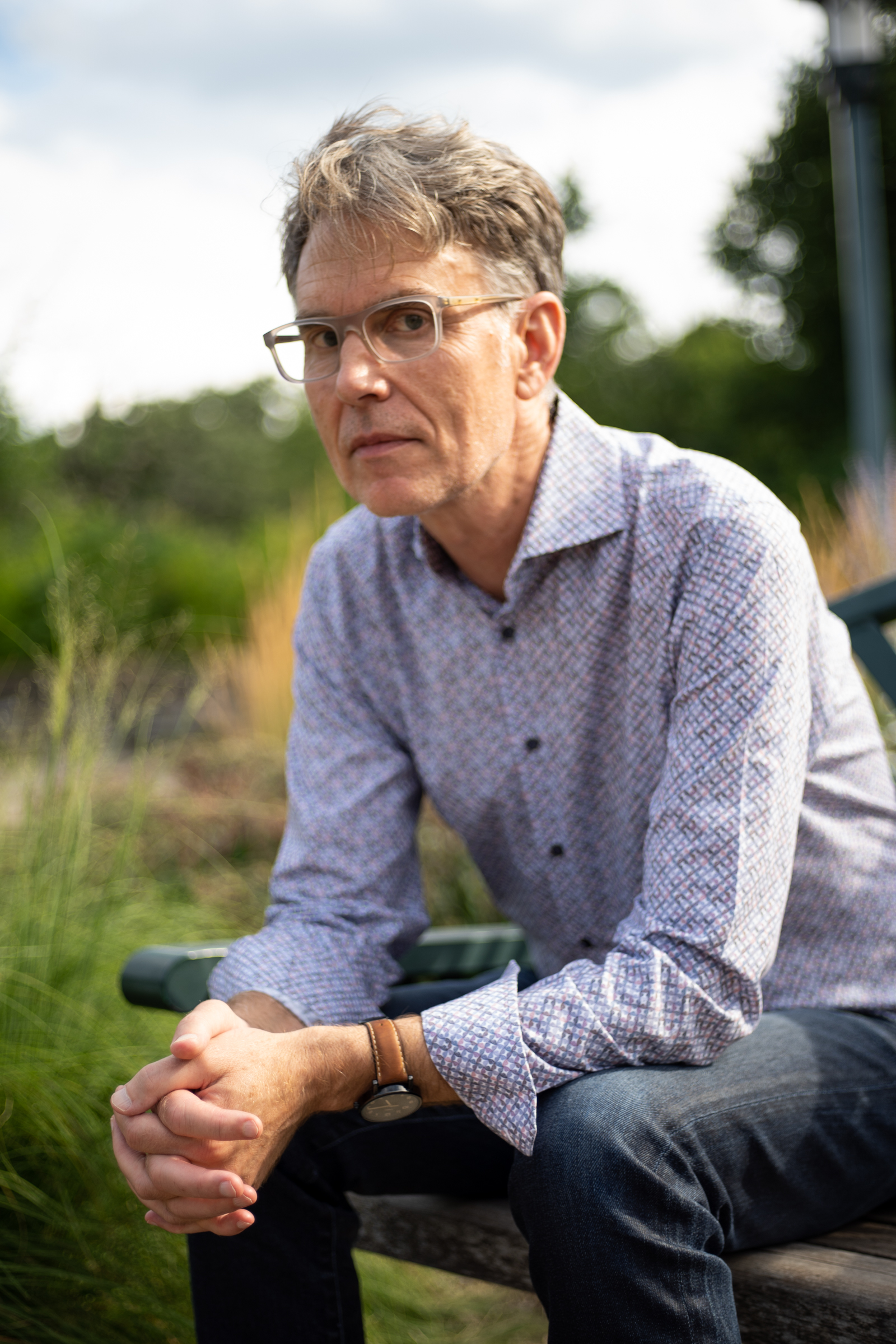 Todd sits on a bench wearing a patterned button down