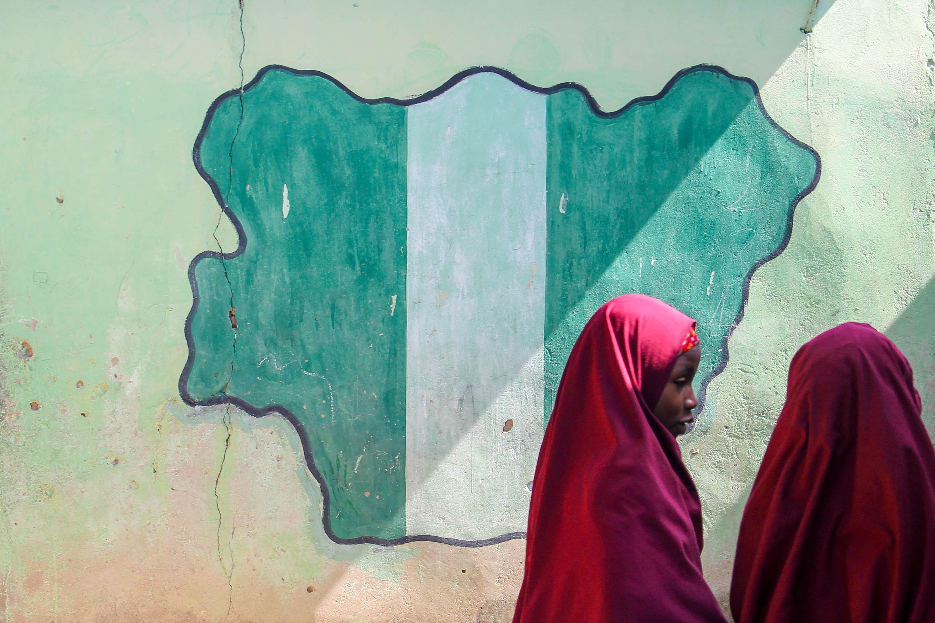 MAIDUGURI, NIGERIA - September 9, 2015: Girl students pass a classroom with the map and flag of Nigeria painted on it, at Success Private School, one of the first schools attacked by Boko Haram in '09. Image by bmszealand/Shutterstock.