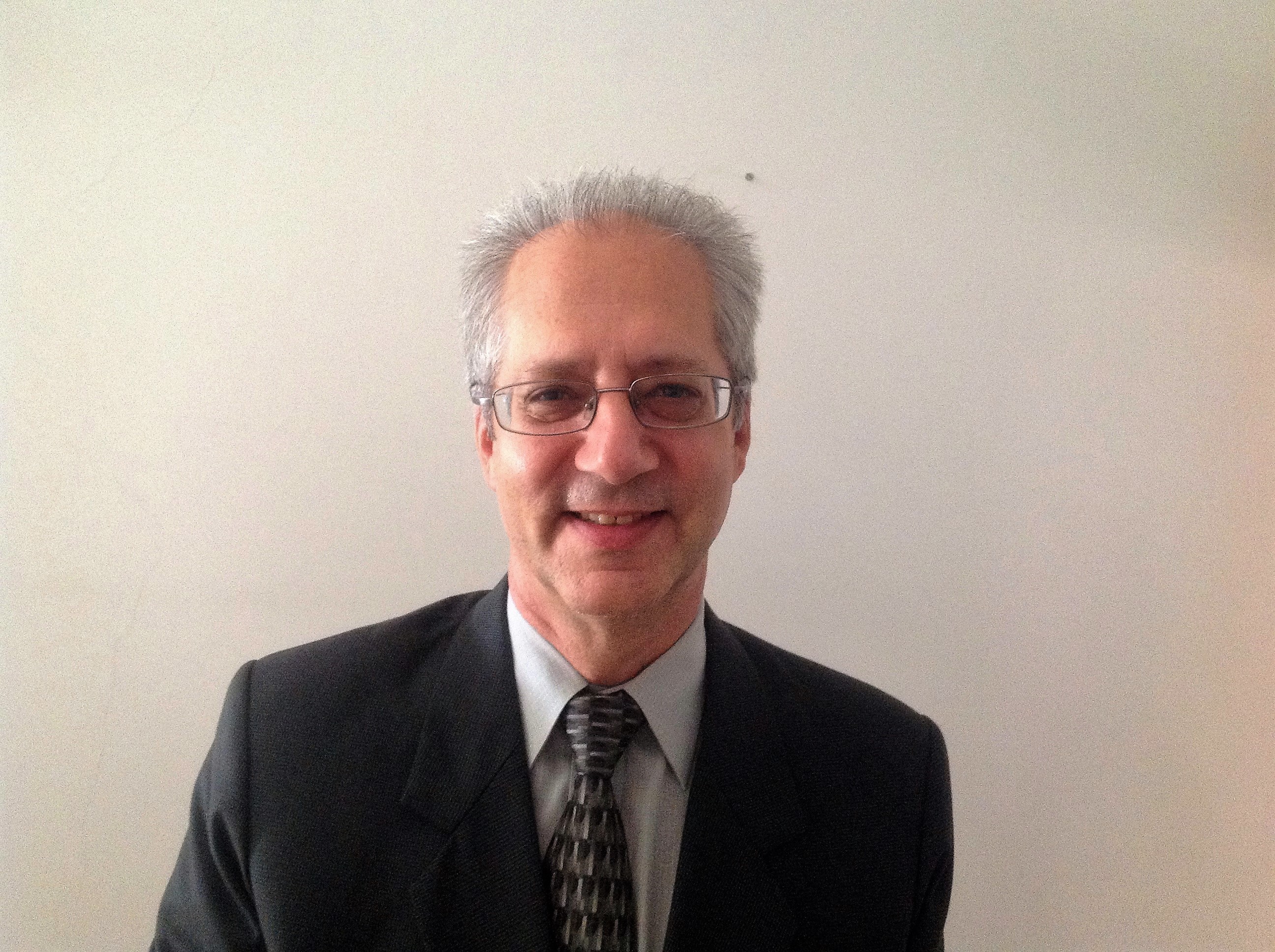 Headshot of Mac wearing a suit and tie against a white background