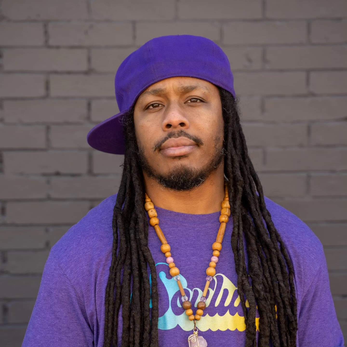 headshot of Montu Miller, who wears a purple t-shirt and hat