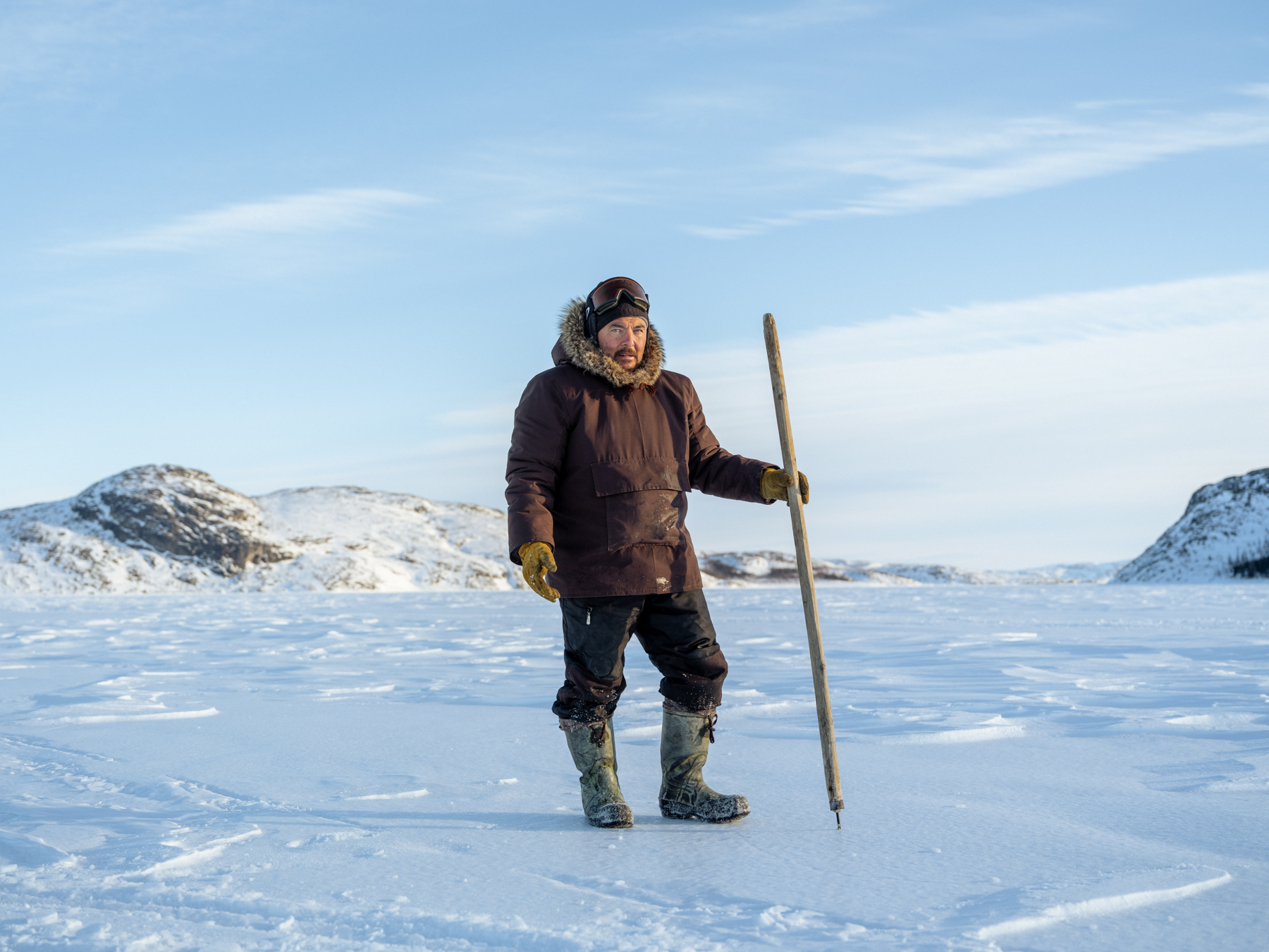 Inuit Project Page1 A man holding a long tool stands in an icy field.
