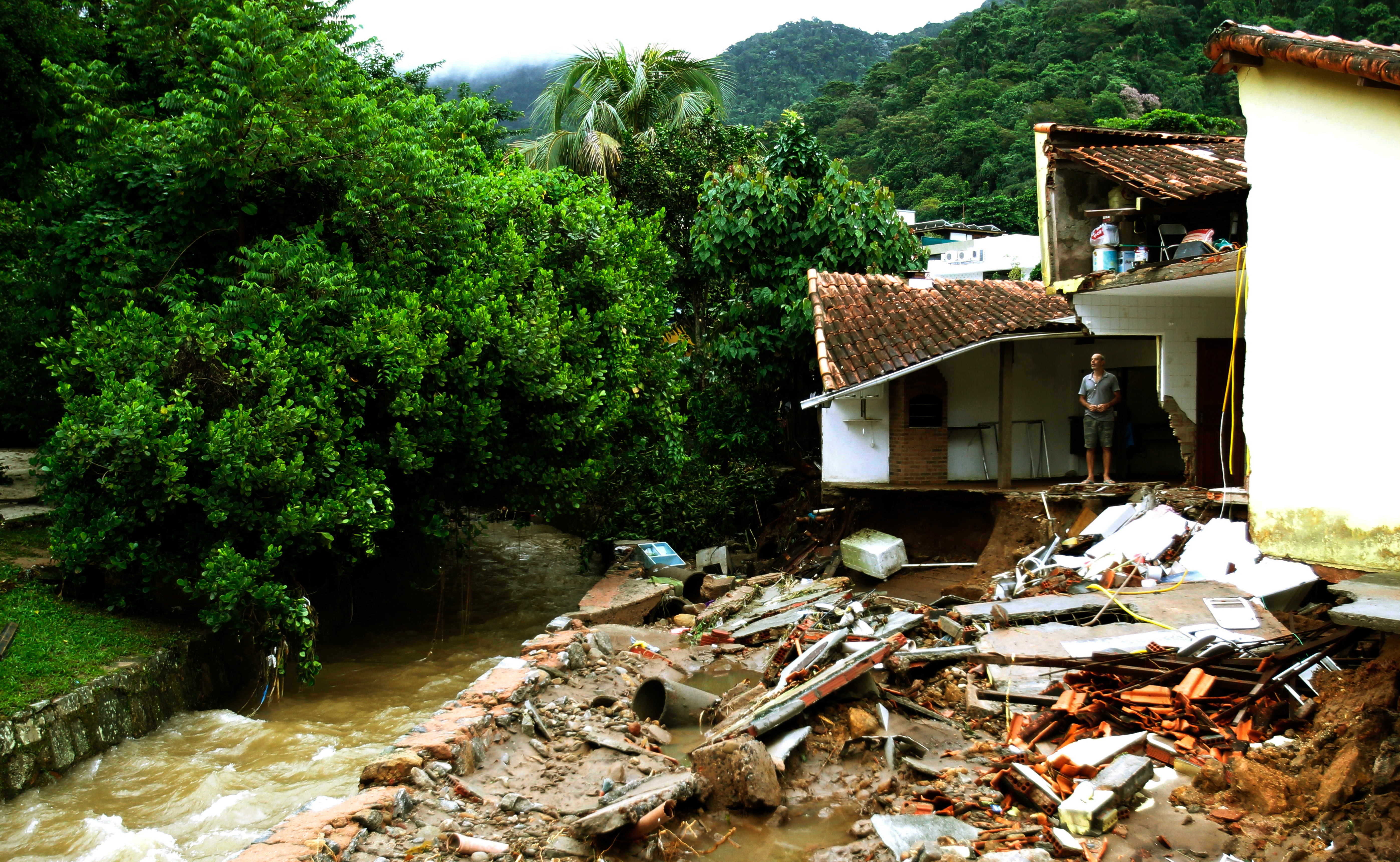 Rio de Janeiro, Brazil April 09, 2019 a man observes the debris of their house in Rio de Janeiro where 10 people dead on April 08 and 09 due to strong rains. Image by Antonio Scorza/Shutterstock.
