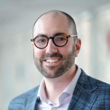 Headshot of man in blue suit and round glasses