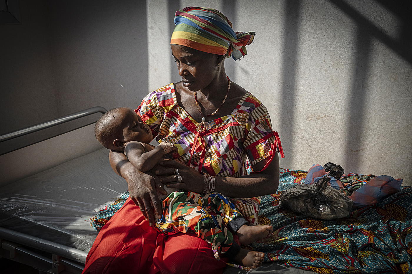 A mother sits on a bed holding her baby