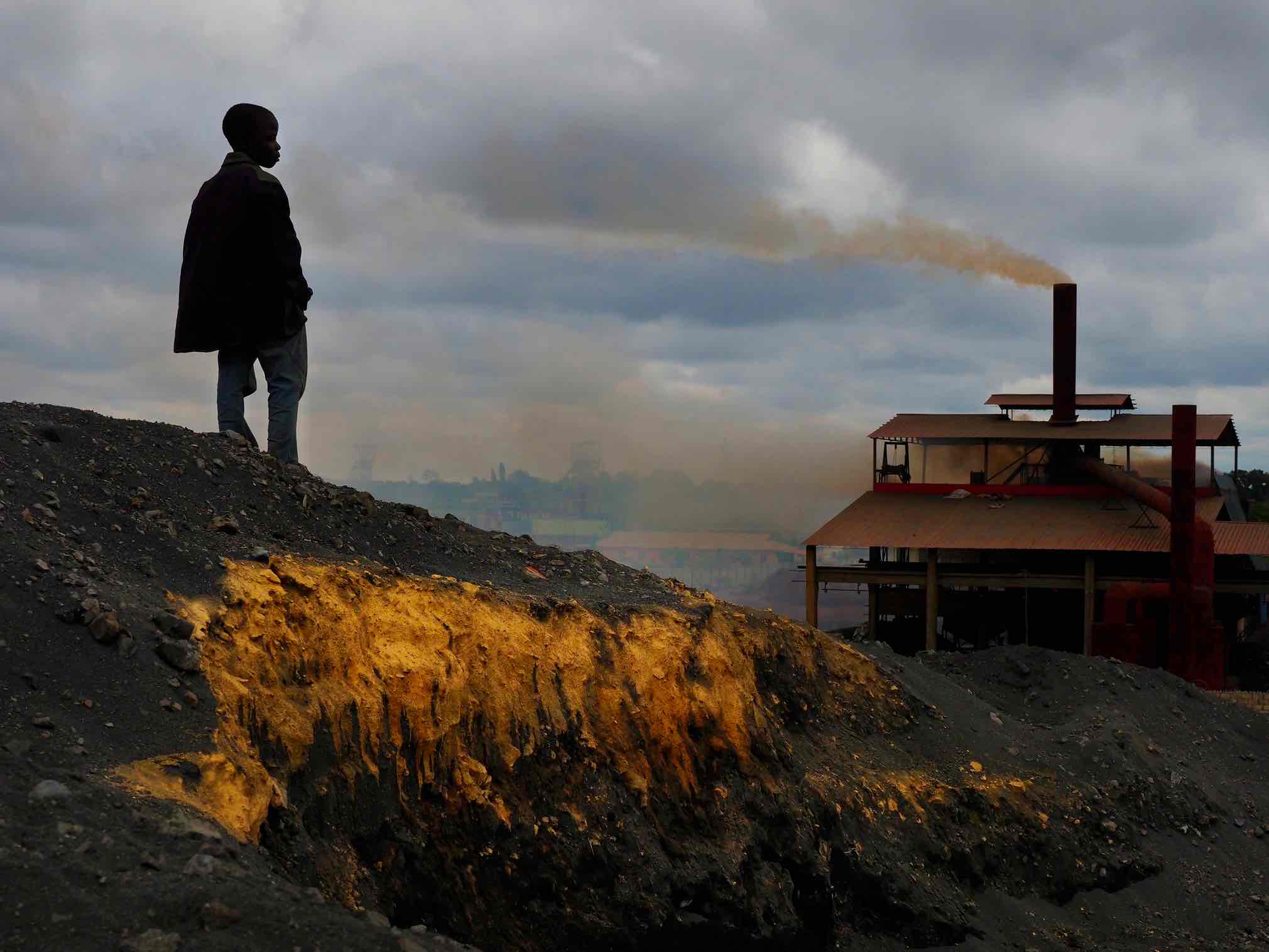Atop Black MountainMore than 6 million metric tonnes of lead slag form Black Mountain, a 30-meter pile of toxic lead waste that still contains a sizable quantity of lead, copper, manganese and zinc. Due to a depressed economy and lack of employment among many of Kabwe's residents, scavengers toil daily to mine some of the richer veins of lead slag for resale to reprocessing smelters in Zambia. The work is dangerous and sometimes deadly. Weak tunnels are dug to reach the brown layers of slag, which miners claim have a higher lead content. Children work among adults in this area at the base of an operating manganese reprocessing smelter managed by the Chinese company Super Deal. The smelter burns lead and manganese slag and spews toxic fumes across the Kabwe area. Image by Larry C. Price. Zambia, 2017. Atop Black Mountain
More than 6 million metric tonnes of lead slag form Black Mountain, a 30-meter pile of toxic lead waste that still contains a sizable quantity of lead, copper, manganese and zinc. Due to a depressed economy and lack of employment among many of Kabwe's residents, scavengers toil daily to mine some of the richer veins of lead slag for resale to reprocessing smelters in Zambia. The work is dangerous and sometimes deadly. Weak tunnels are dug to reach the brown layers of slag, which…