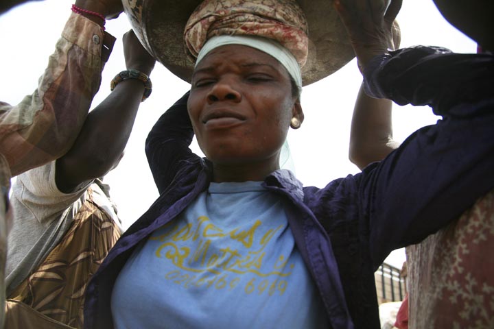 In Agbogbloshie Market, a load of yams is lifted onto the head of 25-year-old Lamisi from Tumu in the Upper West Region, February 13th, 2009. Lamisi is a high school graduate, but with few options for employment in Tumu, she traveled hundreds of miles to Accra to find work. Image by Peter DiCampo. Ghana, 2009. Media file: 5.jpg