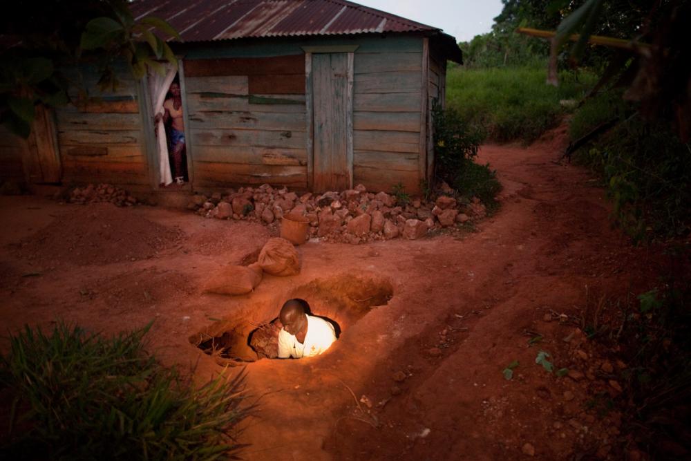 Arnolt Jean looks into a tunnel dug next to a home in Lakwév, Haiti. Jean says walking or running in the community at night is dangerous because of all the holes. People in this village have been digging for gold since the 1960s, and now that gold prices have increased, more of the population has turned to digging. Image by Ben Depp. Haiti, 2012. Media file: BENDEPP (2 of 16).jpg