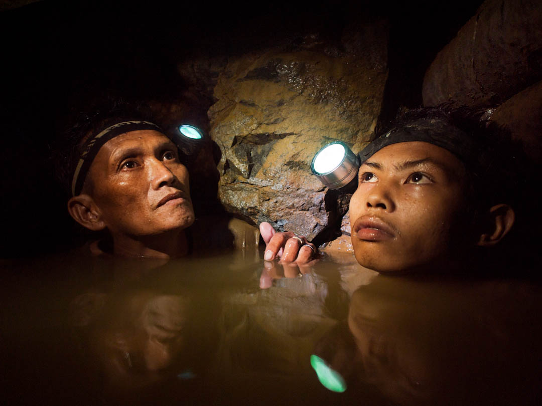 An older miner and a younger boy are chin deep in frigid water 150-meters below the surface as they work a gold mine near Syndicate on the island of Masbate. Image by Larry C. Price. Philippines, 2012. Media file: Price Photo Week Slide Show004.jpg