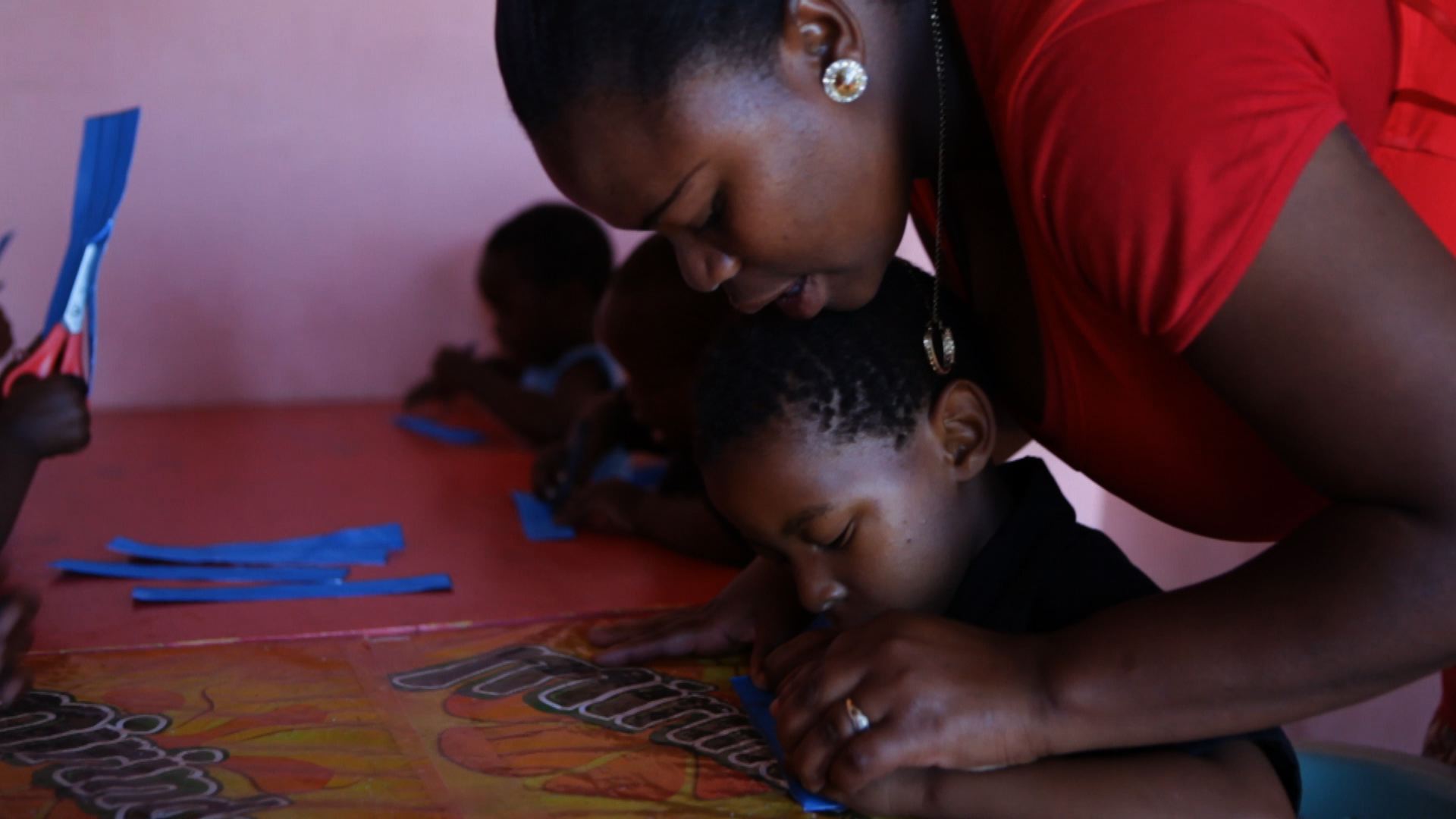 "Aunti Lulu" assists the children in creating a paper garland wreath to decorate the daycare for Christmas. The Raphael Centre sponsors Luleka's daycare by providing teaching materials and art supplies when needed. Image by Samantha Thornton. South Africa, 2012. Media file: StartingYoung_ST_011713_PHOTO.jpg