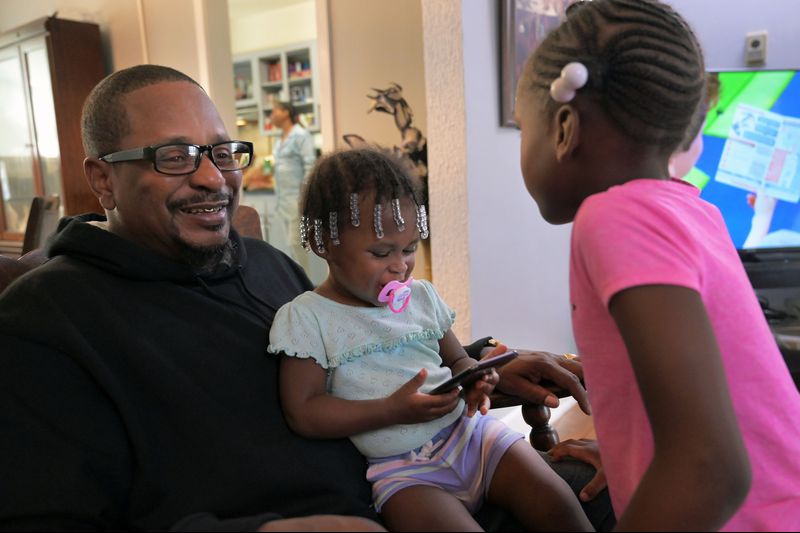 Cecil Burton rocks his granddaughters Chasity Shufford, 1, and Katelyn Ellis, 6, during a family gathering while their mother, Keisha, cooks fried chicken in the kitchen. Burton, 54, said child support once garnished so much of his paycheck he didn't have enough to live on. His coworkers took up a collection for him. Image by Karl Merton Ferron / Baltimore Sun. United States, 2019. Cecil Burton rocks his granddaughters Chasity Shufford, 1, and Katelyn Ellis, 6, during a family gathering while their mother, Keisha, cooks fried chicken in the kitchen. Burton, 54, said child support once garnished so much of his paycheck he didn't have enough to live on. His coworkers took up a collection for him. Image by Karl Merton Ferron / Baltimore Sun. United States, 2019.