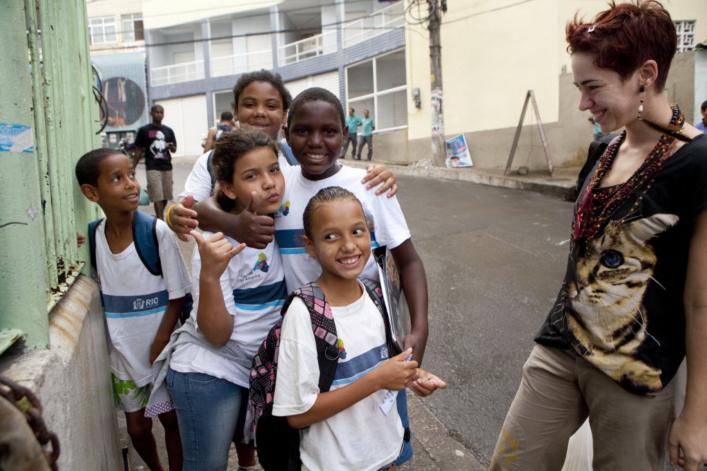 Tatiana Coelho chats with schoolchildren in the Rio de Janeiro favela she now calls home. Coelho, who is Portuguese, came to Brazil a year ago because of all the job opportunities - and because of the weak economy back home. She is an artist. She says she enjoys living in the favela because there is more humanity here, that it is real life. Image by Melanie Stetson Freeman. Brazil, 2012 Media file: favela_tatiana.jpg