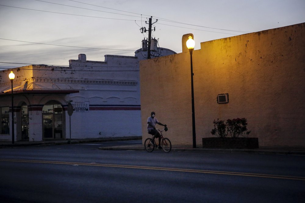 A man riding a bicycle down an empty street wears a protective mask amid the COVID-19 coronavirus outbreak on Friday, April 17, 2020, in Dawson, Ga. Image by Brynn Anderson / AP Photo. United States, 2020. A man riding a bicycle down an empty street wears a protective mask amid the COVID-19 coronavirus outbreak on Friday, April 17, 2020, in Dawson, Ga. Image by Brynn Anderson / AP Photo. United States, 2020.