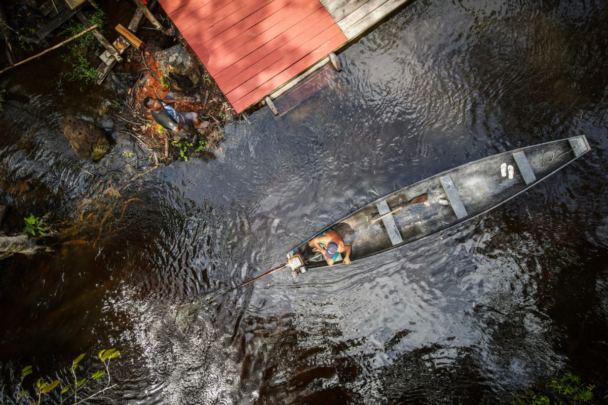 Aerial view of a person in a boat in a river and a person standing on a dock.