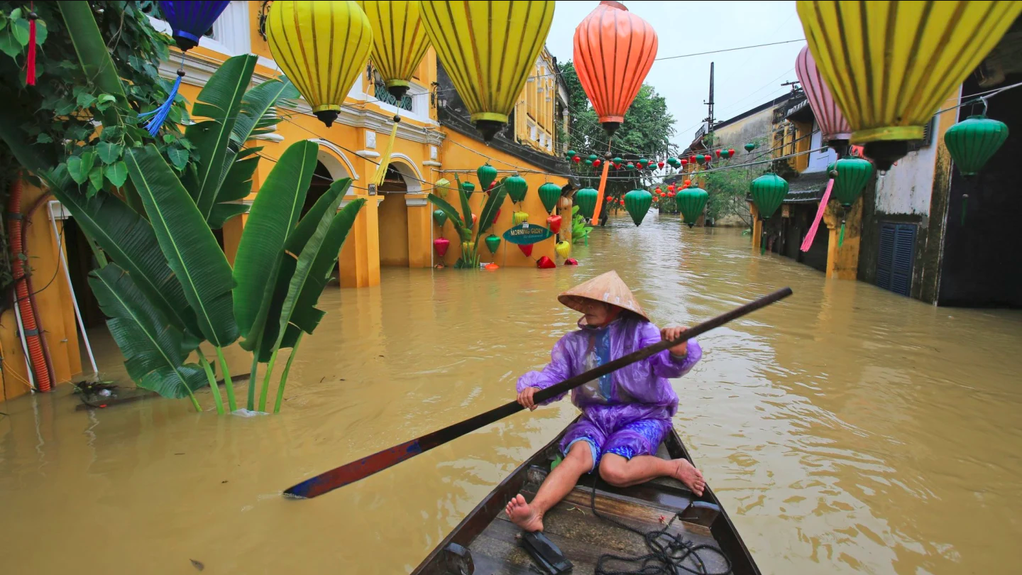 a woman uses an oar to navigate her boat in a flooded street