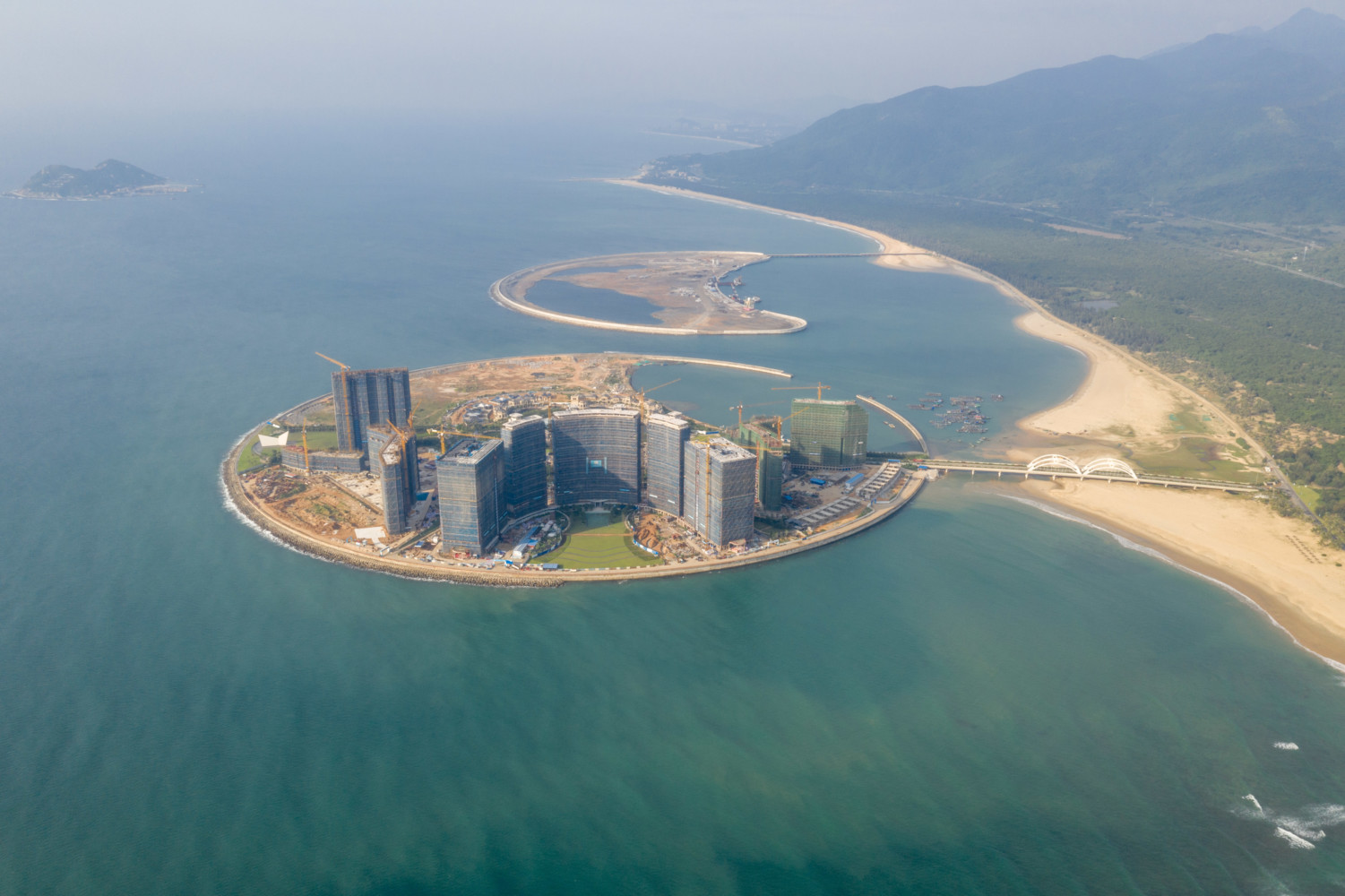 Two islands in the shape of the sun and a crescent moon have been artificially made off Hainan’s east coast, in the Sun and Moon Bay (Riyuewan), a surfing destination 25 km south of Wanning city. The two man-made islands make up about 1 square kilometre, and are planned as a tourism site with a theme park, international conference venues, shopping malls, yacht club and luxury hotels.The land reclamation on the main island—that resembles a round sun—was completed in 2014 and beach erosion was found soon after. The erosion poses a threat to a forest of Vatica Mangachapoi which grows on sandy beaches in Hainan. The endangered plant is protected in China as it has already suffered over-cutting for its valuable wood. In addition, the reclamation project will destroy 50,000 sqm coral reef. Chinese press reports say the project started without carrying out a thorough environmental impact assessment. When these photographs were made in October 2018, construction appeared to still be going on. Italy-based design and… Two islands in the shape of the sun and a crescent moon have been artificially made off Hainan’s east coast, in the Sun and Moon Bay (Riyuewan), a surfing destination 25 km south of Wanning city. The two man-made islands make up about 1 square kilometre, and are planned as a tourism site with a theme park, international conference venues, shopping malls, yacht club and luxury hotels.The land reclamation on the main island—that resembles a round sun—was completed in 2014 and beach erosion was found soon…