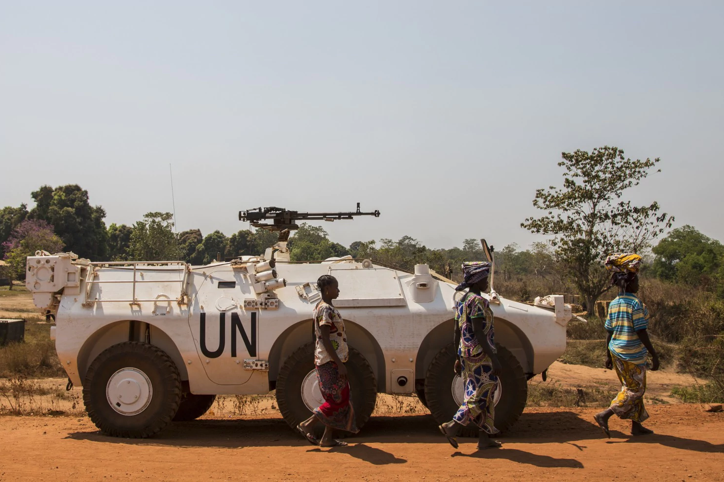 Women walk past a U.N. vehicle at the entrance to the sprawling camp in Kaga-Bandoro for thousands of families displaced by civil conflict. Image by Jack Losh. Central African Republic, 2018. Women walk past a U.N. vehicle at the entrance to the sprawling camp in Kaga-Bandoro for thousands of families displaced by civil conflict. Image by Jack Losh. Central African Republic, 2018.