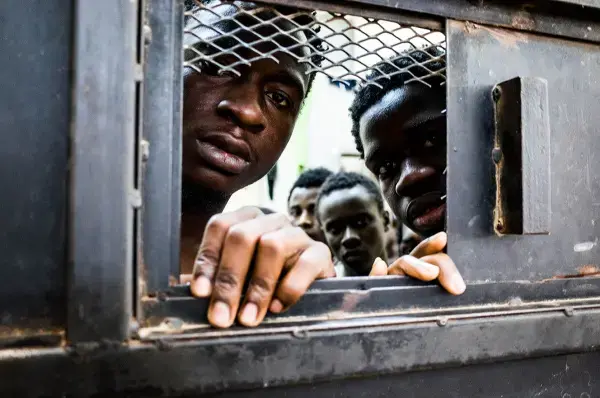 Detainees from West Africa peer out of their overcrowded cell in the Nasr detention center in Zawiya, where migrants intercepted by the coast guard are warehoused indefinitely. Image by Peter Tinti. Libya, 2017.