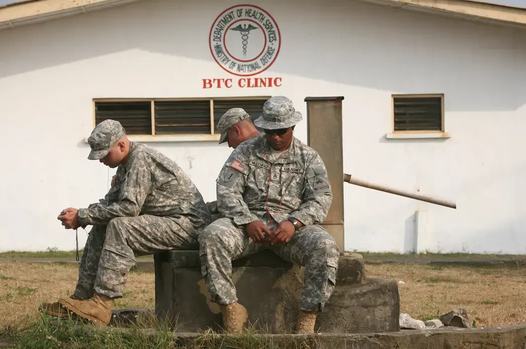 Spc. Kyle Salchow, from Nixa, Mo., Spc. Eric Warford, from Denver, Co., and Staff Sgt. Jose Melendez from Fajardo, Puerto Rico, wait for a bus ride off Barclay Training Center in Monrovia. These soldiers are part of the 2,500 U.S. troops in Operation United Assistance that is building Emergency Treatment Units and training local health care workers in Liberia. They are among the 20 percent of the force that is deploying home at the beginning of January 2015. Photo by Cheryl Hatch/ZUMA Press. Liberia, 2014. Media file: waiting_5782_300.jpg