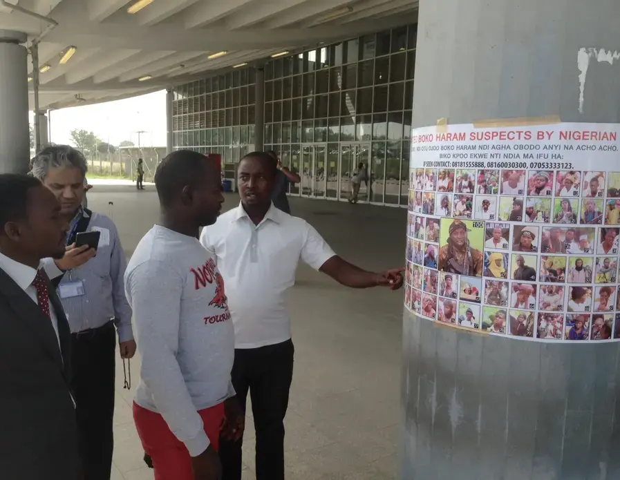 Travelers examine a most wanted poster featuring Boko Haram suspects at an airport near the Nigerian capital. Image by Jason Motlagh. November 2015. Travelers examine a most wanted poster featuring Boko Haram suspects at an airport near the Nigerian capital. Image by Jason Motlagh. November 2015.