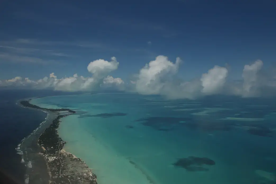 More than half of Kiribati’s 110,000 people live on the capital island of Tarawa. It’s a heavily developed string of islets connected by causeways in various states of disrepair. The deep blue Pacific Ocean sits on one side, the shallow aquamarine lagoon on the other. From any place on the atoll, the water is always a short walk away. Image by Kenneth R. Weiss. Kiribati, 2014. Media file: img_8504.jpg