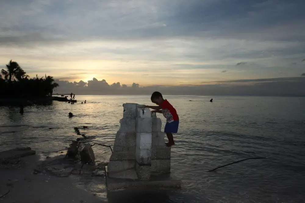 Four-year-old Aberam Maerere plays on the concrete block corner of a house that was claimed by the sea. The community of Te Bikenikora has lost dozens of homes in recent years to erosion and the advancing sea. The local church has elevated its foundation by 18 inches so parishioners could stay dry at high tide. Image by Kenneth R. Weiss. Kiribati, 2014. Media file: img_4753.jpg