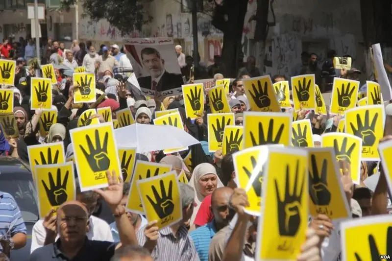 Demonstrators hold up four fingers, a symbol of their solidarity with the the destroyed sit-in protest known as Rabaa, which means four or fourth in Arabic, Cairo, August 23, 2013. Image by H. Elrasam for VOA. Courtesy of Wikimedia Commons. Egypt, 2013. Media file: r4bia_sign_used_in_solidarity_with_victims_of_rabaa_crackdown_23-aug-2013.jpg