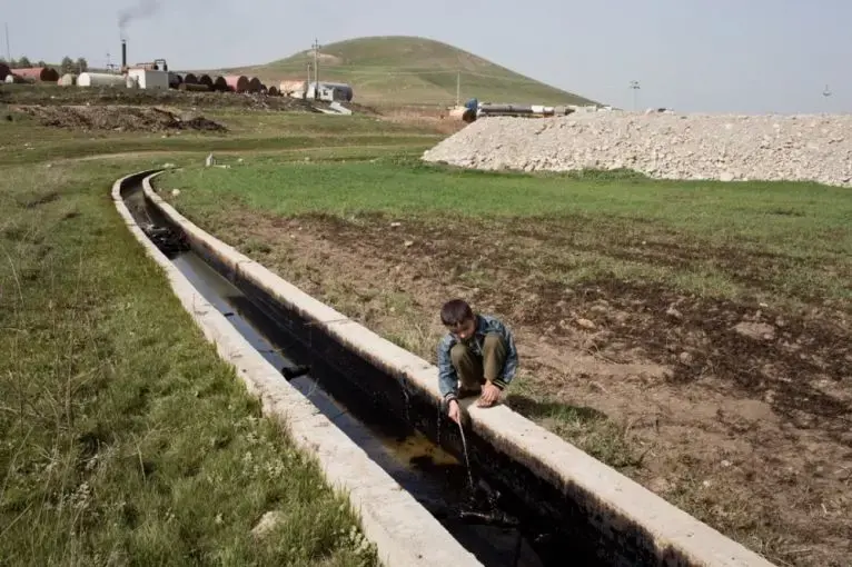 Ezidiar, 9, plays with an oil slick running through the agricultural land below the refinery. Image by Sebastian Meyer. Iraq, 2015.