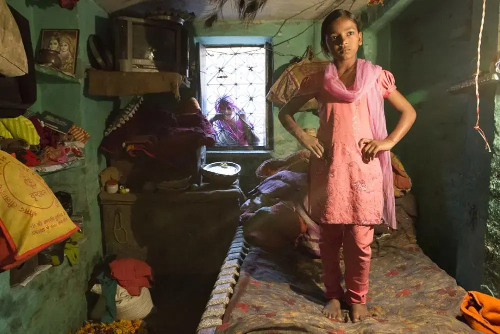 Gunjan’s older sister Tanuja tries on her best outfit prior to going to a family wedding. At 13-years-old and unmarried, her mother keeps her inside most of the time for fear that she will get hurt or taken in the streets. In conservative parts of India and especially in their neighborhood, a girl is expected to get married at puberty but her mother, a widow, will struggle to find any of her three daughters respectable suitors without money for the dowries. Image by Amy Toensing. India, 2013. Media file: toensing_20131122_10466.jpg
